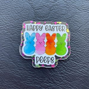 Könnte beinhalten: Ein klarer, rechteckiger Anstecker mit den Worten "HAPPY EASTER" und "PEEPS" in Weiß. Der Anstecker zeigt vier bunte Marshmallow-Peeps: blau, rosa, orange und grün. Der Anstecker ist mit einem glitzernden Rand versehen.