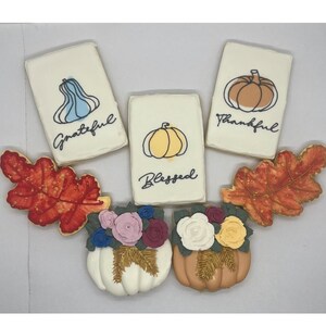 May include: A selection of autumn-themed decorated biscuits. Rectangular biscuits feature pumpkin and gourd illustrations with the words "Grateful," "Blessed," and "Thankful." Pumpkin-shaped biscuits are decorated with flowers and leaves.