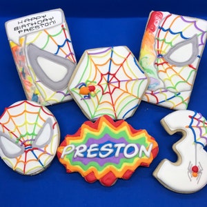 May include: Six decorated sugar cookies with a rainbow theme. The cookies feature a spiderweb design, a spider, the number 3, and the name Preston. One cookie says "Happy Birthday Preston".