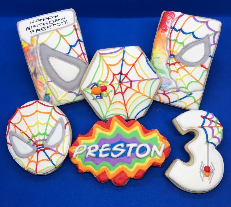 May include: Six decorated sugar cookies with a rainbow theme. The cookies feature a spiderweb design, a spider, the number 3, and the name Preston. One cookie says "Happy Birthday Preston".