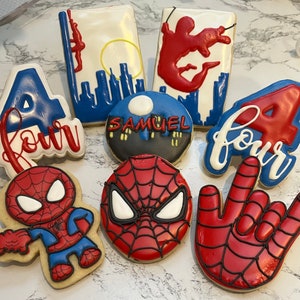 May include: A set of ten decorated sugar cookies featuring a Spiderman theme. The cookies are decorated with red, blue, and white icing. The cookies feature the number four, the words "four", a Spiderman mask, and a Spiderman hand.