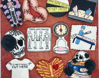 May include: A set of ten decorated sugar cookies with various themes, including a heart with stitches, a skull with a spiderweb, a scale with a brain, and a crime scene tape. The cookies are decorated with colourful icing and details.