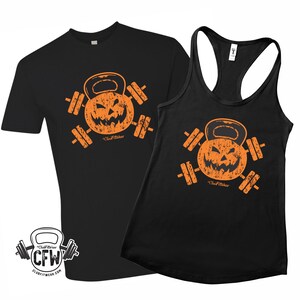 以下が含まれることがあります： 黒のTシャツとタンクトップに、くすんだオレンジ色のジャック・オ・ランタンのケトルベルとダンベルのグラフィックがプリントされています。グラフィックには「ClubFitWear」の文字があります。