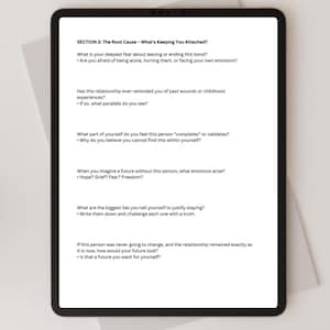 May include: A black tablet displaying text from "SECTION 3: The Root Cause - What's Keeping You Attached?" The text includes questions about relationships, fears, and self-reflection. The tablet is on a white surface.