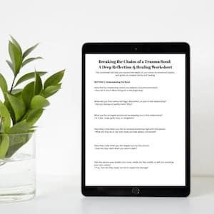 May include: A black tablet displays a worksheet titled "Breaking the Chains of a Trauma Bond." The worksheet explores emotional impact and healing. A glass vase with green leaves is on the left. The text includes questions about relationships and emotional ties.