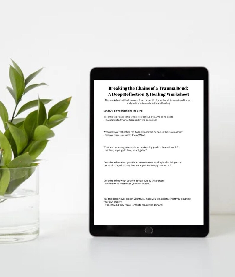 May include: A black tablet displays a worksheet titled "Breaking the Chains of a Trauma Bond." The worksheet explores emotional impact and healing. A glass vase with green leaves is on the left. The text includes questions about relationships and emotional ties.