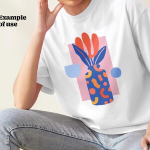 Puede incluir: Camiseta blanca con un dise&ntilde;o gr&aacute;fico de un jarr&oacute;n azul con formas abstractas naranjas y amarillas y una planta roja y verde. El jarr&oacute;n est&aacute; sobre un fondo rosa con c&iacute;rculos azules y blancos.