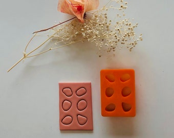 Puede incluir: Dos moldes de silicona naranja para hacer fondant o arcilla polimérica. Los moldes son rectangulares y presentan seis formas diferentes de pequeñas piedras redondeadas.