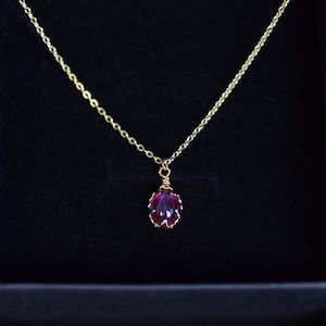 May include: A gold chain necklace with a deep red gemstone pendant. The pendant is set in a gold wire frame.