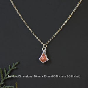 May include: A silver-toned chain necklace featuring a small, teardrop-shaped orange gemstone pendant encased in a silver wire cage. The pendant measures 0.39 inches by 0.51 inches. The necklace is displayed against a dark, solid background.