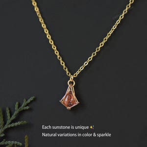 May include: A gold-toned chain necklace featuring a teardrop-shaped sunstone pendant encased in a geometric wire frame. The text on the image reads: Each sunstone is unique. Natural variations in color & sparkle.