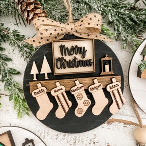 May include: Black wooden Christmas ornament with a burlap bow and the words "Merry Christmas" in a square. The ornament has five stockings with the names "Daddy", "Mama", "Abraham", "Abigail", and "Adam" written on them.