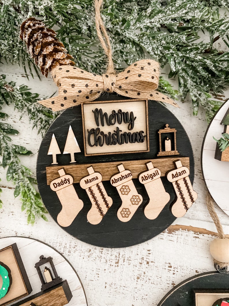 May include: Black wooden Christmas ornament with a burlap bow and the words "Merry Christmas" in a square. The ornament has five stockings with the names "Daddy", "Mama", "Abraham", "Abigail", and "Adam" written on them.