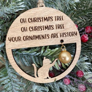 May include: Wooden Christmas ornament with a cat silhouette and the text "Oh Christmas Tree Oh Christmas Tree Your Ornaments Are History".