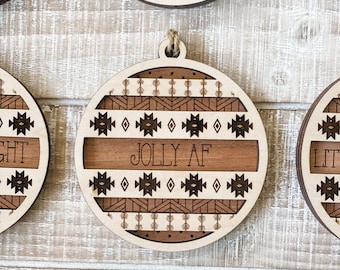 May include: A circular wooden Christmas ornament featuring a layered design with laser-cut geometric patterns in dark brown and light natural wood. The centre horizontal band displays the text JOLLY AF in a simple, dark, sans-serif font.