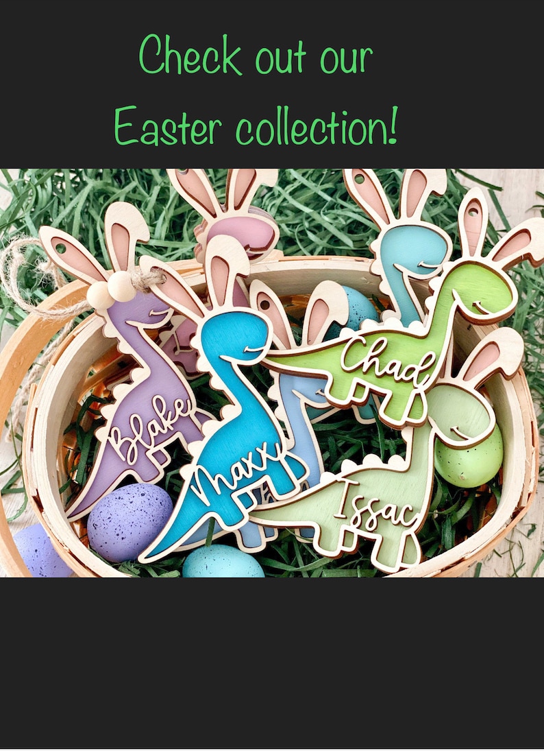 May include: Five wooden dinosaur-shaped Easter decorations with bunny ears. The dinosaurs are painted in various pastel colours and have names written on them: Blake, Maxx, Chad, Issac. The decorations are in a basket filled with green grass.