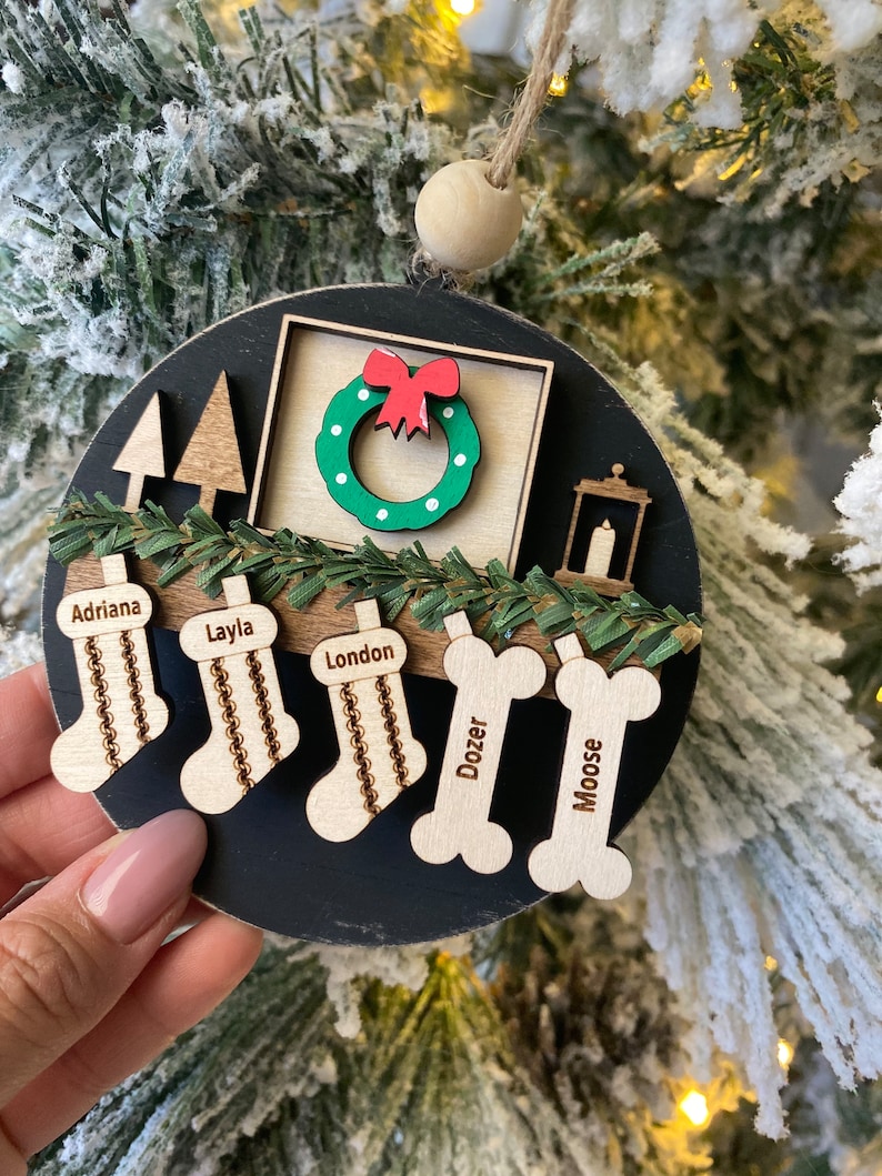 May include: A black and white Christmas ornament with a wreath, a lantern, and stockings with the names Adriana, Layla, London, Dozer, and Moose.