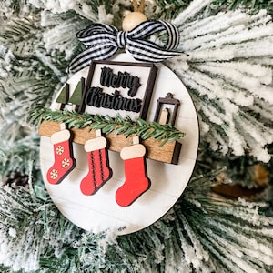 May include: White wooden Christmas ornament with a black and white striped bow, a sign that says "Merry Christmas", and three red stockings hanging from a wooden shelf.