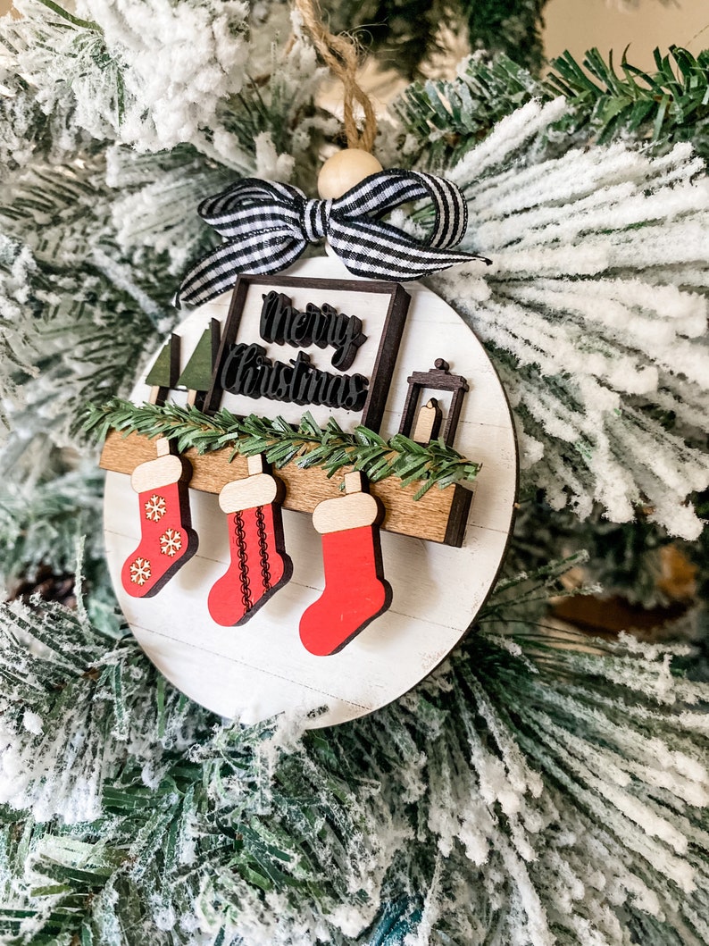 May include: White wooden Christmas ornament with a black and white striped bow, a sign that says "Merry Christmas", and three red stockings hanging from a wooden shelf.