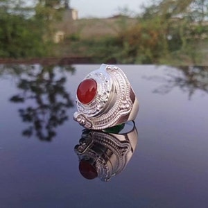 Op de afbeelding: Een zilveren ring met een sierlijk ontwerp en een rode carneol-steen in het midden.