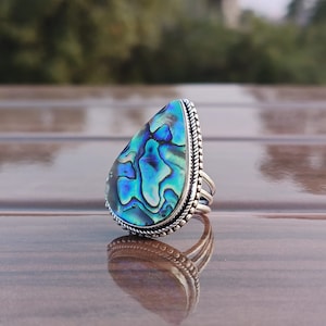 Puede incluir: Un anillo en forma de lágrima con una incrustación de concha de abulón azul y verde engastada en plata.