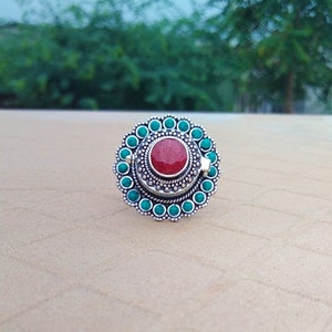 May include: A silver ring with a red stone in the center and a circle of turquoise stones around the edge.