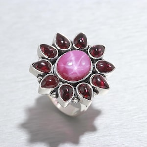 Peut inclure: Une bague en argent avec une pierre rose en forme d'étoile entourée de petites pierres rouges.