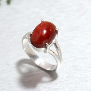 May include: A silver ring with a red oval gemstone set in a prong setting. The ring has a split shank.