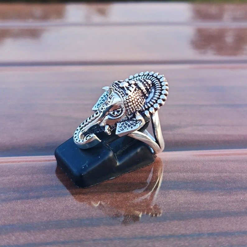 K&ouml;nnte beinhalten: Silberring mit einem aufwendig detaillierten Elefantenkopfdesign. Der Ring befindet sich auf einem schwarzen Ringst&auml;nder.