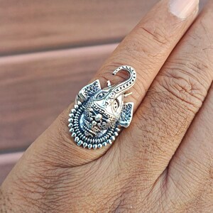 K&ouml;nnte beinhalten: Ein silberner Ring mit einem aufwendig detaillierten Elefantenkopfdesign. Der R&uuml;ssel des Elefanten ist nach oben gerollt, und der Ring hat einen dekorativen Rand.