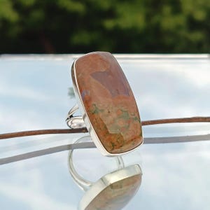May include: A silver ring with a rectangular brown and green gemstone. The gemstone has a unique pattern of swirls and spots.