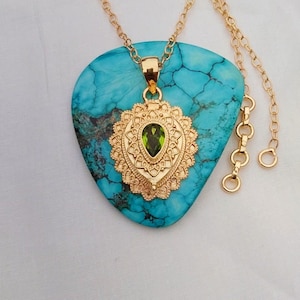 Puede incluir: Un collar de oro con un colgante turquesa que presenta una piedra preciosa verde engastada en un diseño de filigrana.