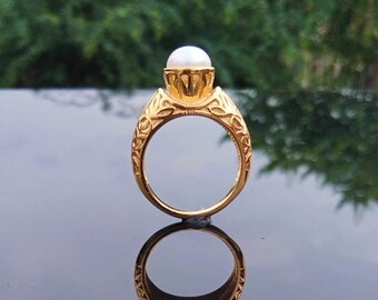 May include: A gold ring with an ornate design and a white pearl in the centre.