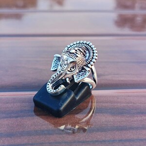 K&ouml;nnte beinhalten: Ein silberner Ring mit einem filigranen Design eines Elefantenkopfes. Der Ring befindet sich auf einem schwarzen Pr&auml;sentationsst&auml;nder.