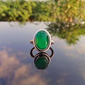 May include: A silver ring with a large, oval-shaped green gemstone. The ring is set in a simple, silver band.