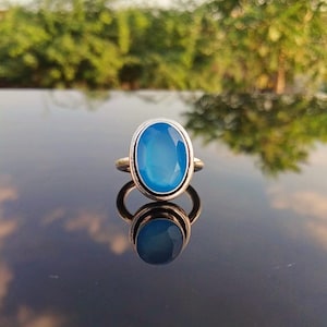 May include: A silver ring with a blue oval gemstone. The ring is set in a simple, elegant design.