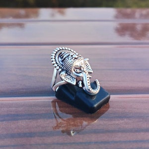 K&ouml;nnte beinhalten: Silberring mit einem verzierten Elefantenkopfdesign. Der Ring befindet sich auf einem schwarzen Pr&auml;sentationsst&auml;nder.
