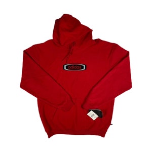 May include: Red hooded sweatshirt with a black and silver adidas logo on the front. The logo is in a rectangular shape with rounded corners and the word "adidas" in red letters.