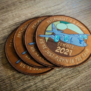 May include: Four brown embroidered patches with a plane and the text "Deployment is a beach. We're just playin' in the sand. Summer 2021."