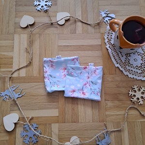 Könnte beinhalten: Zwei blaue Stoff-Teelichthüllen mit einem Blumenmuster aus rosa Blüten auf einer Holzoberfläche mit einer Girlande aus Herzen und Schneeflocken.