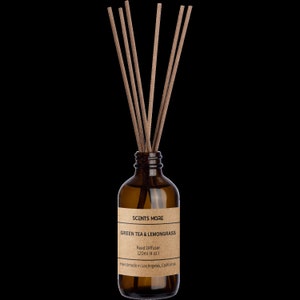 May include: A brown glass bottle with a brown paper label that reads "SCENTS MORE GREEN TEA & LEMONGRASS Reed Diffuser 120ml (4 oz) Handmade in Los Angeles, California". The bottle has brown sticks in it.