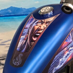 Pode incluir: Um depósito de gasolina azul para motocicleta com um gráfico detalhado de um rosto gritando e um design tribal. A obra de arte apresenta cores vibrantes e uma expressão dramática. O tanque também tem uma tampa de combustível prateada.