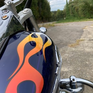 May include: Close-up of a blue motorcycle gas tank with a yellow, orange, and red flame design. The motorcycle is chrome and has a speedometer visible.