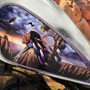 May include: A gas tank decal featuring a Native American man with a headdress, a dramatic landscape, and a pair of eagles flying overhead. The decal is printed on a dark background with a purple border.