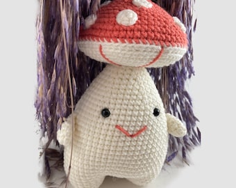 May include: A crocheted mushroom plush toy with a white body and a red and white cap. The toy has a smiling face with black eyes and a red mouth.