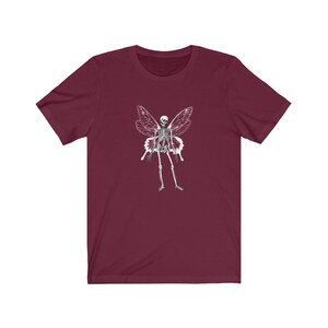 Puede incluir: Una camiseta color burdeos con un gr&aacute;fico blanco de un esqueleto con alas de mariposa.
