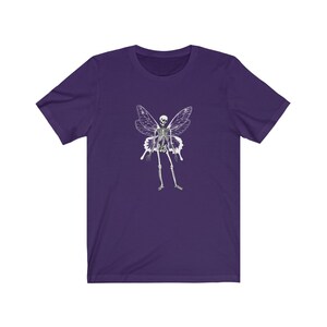 Puede incluir: Camiseta de manga corta de color morado con un gr&aacute;fico blanco de un hada esqueleto con alas.