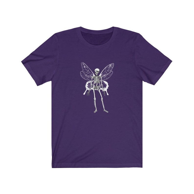 Puede incluir: Camiseta de manga corta de color morado con un gr&aacute;fico blanco de un hada esqueleto con alas.