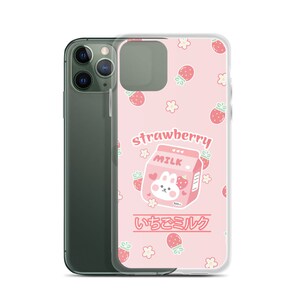 May include: A pink phone case with a cartoon strawberry milk carton and a bunny on it. The case has a white background with pink strawberries and white flowers. The text "strawberry milk" and "いちごミルク" are printed on the case.