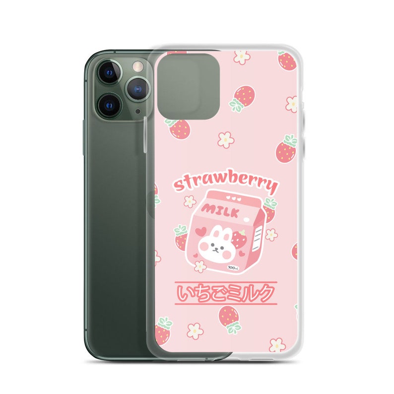 May include: A pink phone case with a cartoon strawberry milk carton and a bunny on it. The case has a white background with pink strawberries and white flowers. The text "strawberry milk" and "いちごミルク" are printed on the case.